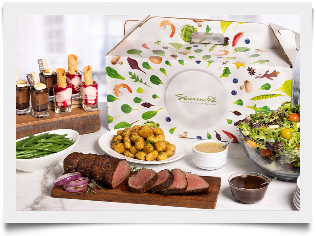 White take-home meal box featuring assorted green illustrated ingredients and the Seasons52 logo prominently centered.